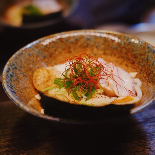A close-up shot of a perfectly cooked ramen bowl with chashu pork, a soft-boiled egg, and green onions, steamy and inviting, reminiscent of a scene from a Japanese drama.