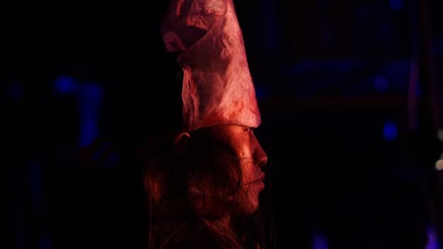 A close-up shot of a theatrical stage, dimly lit, with a single actor in a moment of intense emotional expression, symbolizing the raw vulnerability and power of drama to convey social truths.